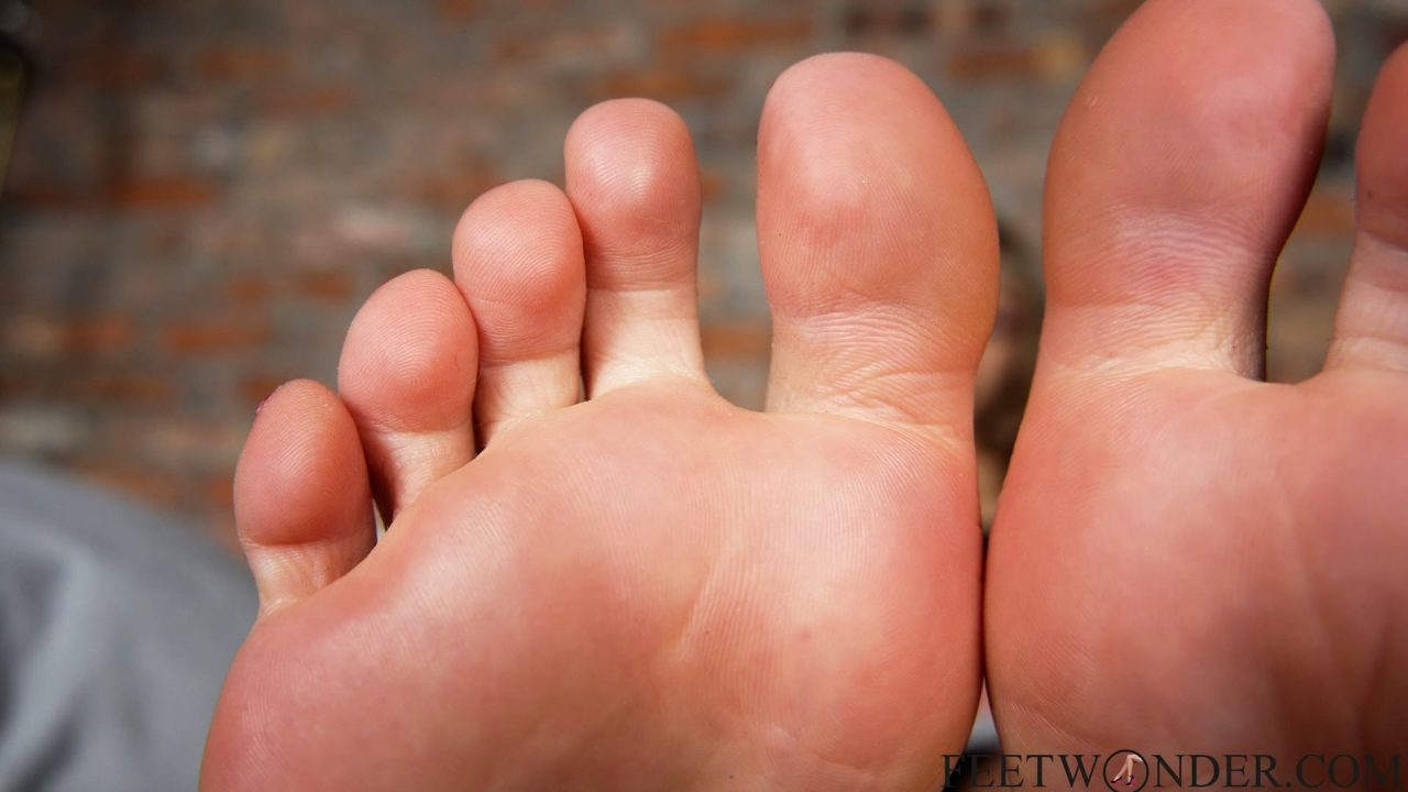 Wrinkled bare soles and toes pressed close to camera over grey blanket